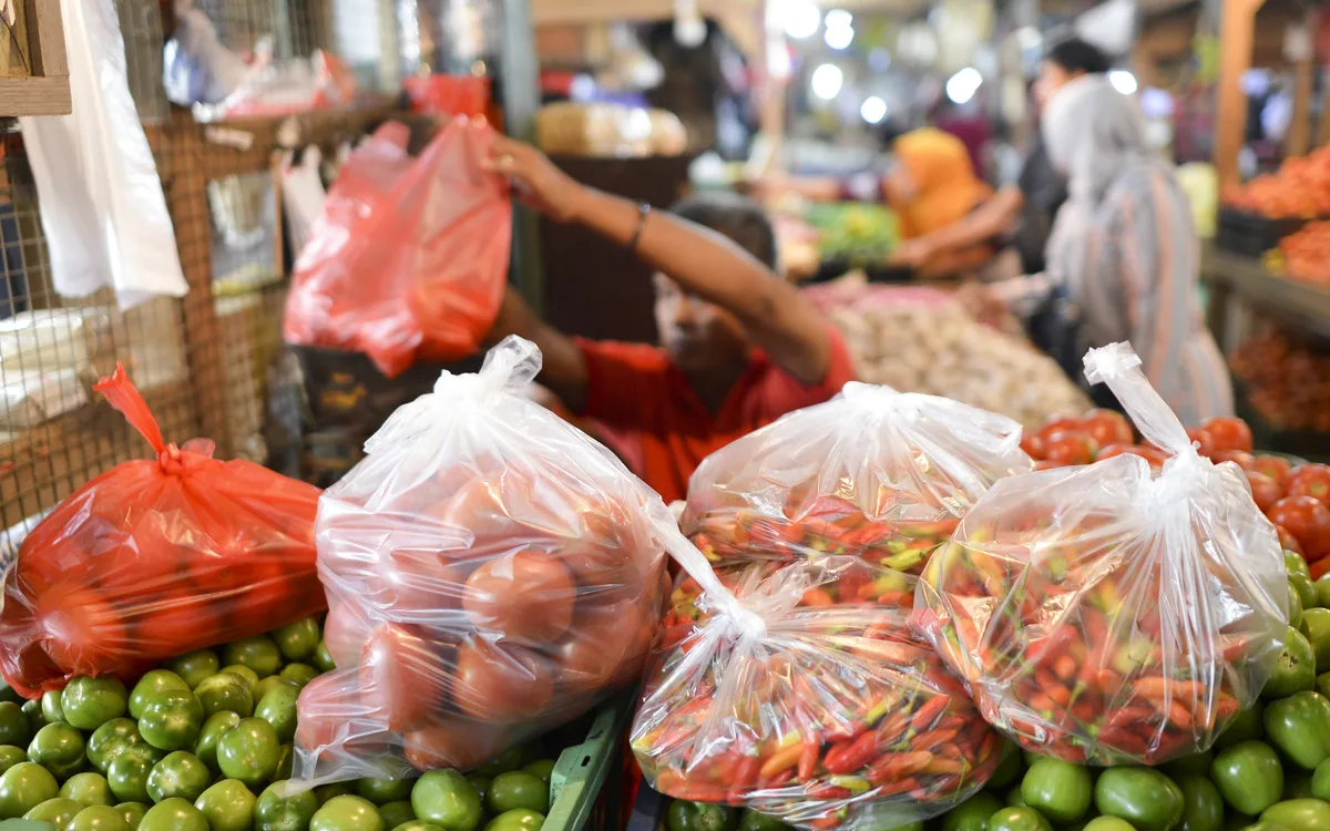 Vendor at a wet market bagging produce in single-use plastic bags